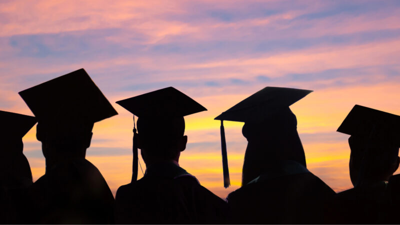 Students wearing graduation caps in silhouette against a sunset.