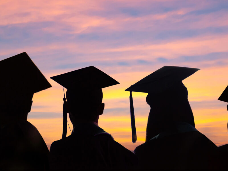 Students wearing graduation caps in silhouette against a sunset.